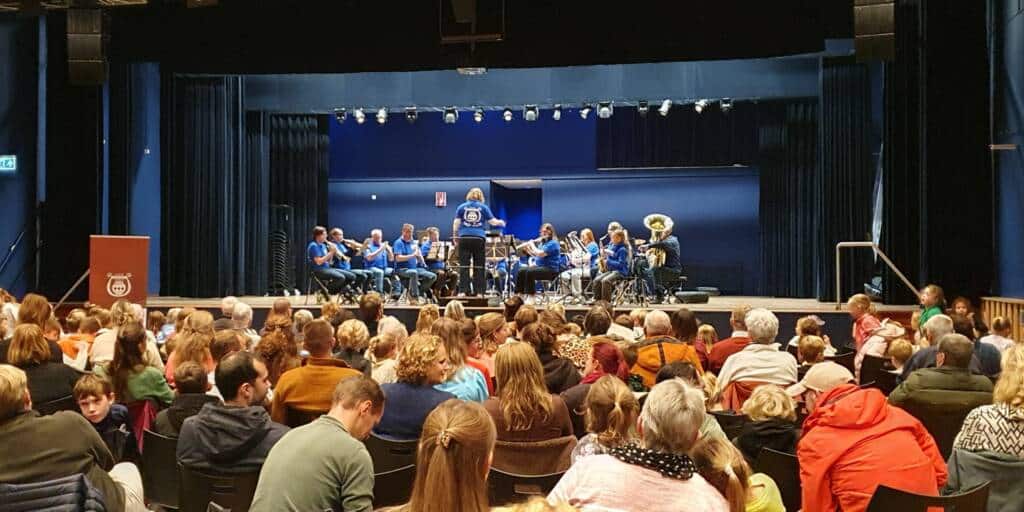 Donderdagavond 30 oktober 2025; 19:00 uur … een stormvloed aan opa’s, oma’s, broertjes, zusjes, vaders, moeders en vriendjes en vriendinnetjes kwam de grote zaal van De Drie Linden binnen. In allerijl werden extra stoelen geplaatst. Wat was er aan de hand? Het flink gegroeide Opleidingsorkest van Amor Musae verzorgde er een concert. Onder leiding van dirigente Judith van Boven werd het moment gevierd dat een scholenproject “Blaasmuziek is Cool” werd afgerond. Een project dat wordt verzorgd door Nieuwe Veste op basisschool De Horizon.